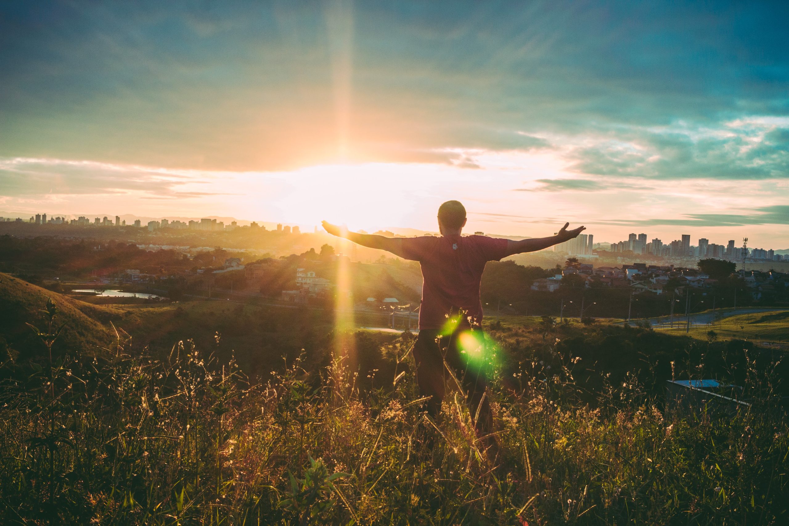 person on a hilltop at sunset with arms outstretched
